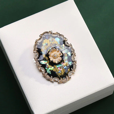 Agatha Resin Cameo Brooch - A round oval-shaped brooch with a black background, with layers of gold enamel paint, abalone shell, and resin, and a pretty stylised sunflower in the centre like a shield.