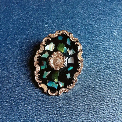 Agatha Resin Cameo Brooch - A round oval-shaped brooch with a black background, with layers of gold enamel paint, abalone shell, and resin, and a pretty stylised sunflower in the centre like a shield.