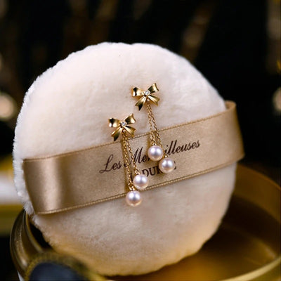 Audrey Bow Tassel Earrings - Tiny, delicate gold earrings shaped like stylised bows, with two tiny pearls suspended from fine gold chains below the lobe.