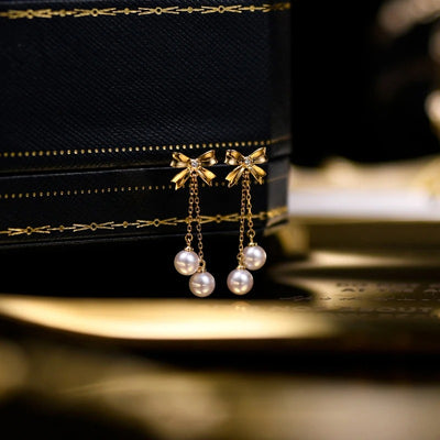 Audrey Bow Tassel Earrings - Tiny, delicate gold earrings shaped like stylised bows, with two tiny pearls suspended from fine gold chains below the lobe.