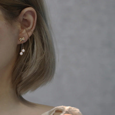 Audrey Bow Tassel Earrings - Tiny, delicate gold earrings shaped like stylised bows, with two tiny pearls suspended from fine gold chains below the lobe.