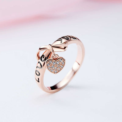 Be Still My Heart Ring - A rose gold ring with a heart and ribbon theme.