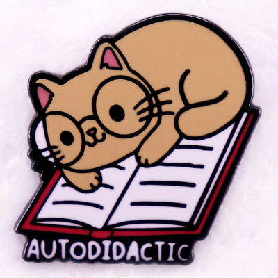 The "Autodidactic" Enamel Pin is a tiny, adorable enamel pin, featuring cute little kitty with big, round glasses reading a book, and the word "Autodidactic" alone the bottom in very small letters.