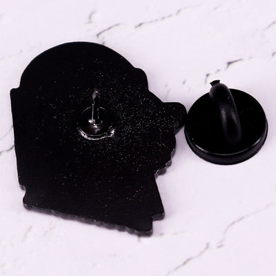 The "Autodidactic" Enamel Pin is a tiny, adorable enamel pin, featuring cute little kitty with big, round glasses reading a book, and the word "Autodidactic" alone the bottom in very small letters.