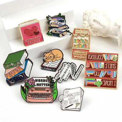 The "Autodidactic" Enamel Pin is a tiny, adorable enamel pin, featuring cute little kitty with big, round glasses reading a book, and the word "Autodidactic" alone the bottom in very small letters.