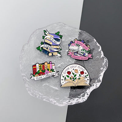 The "Book And Flower Lover" Enamel Pin is a tiny, but very stylish enamel pin, featuring a pile of stylised books wreathed in flowers and ribbons, along with simple letters proclaiming your love of said books and flowers. So cute! Grab yours today!