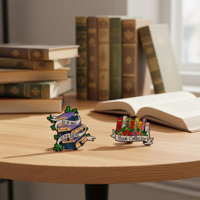 The "Book Collector" Enamel Pin is an adorable, teeny-tiny little enamel pin, featuring a row of stylised books in shades of pink, orange, and red, adorned with flowers and ribbons. So cute! Grab yours today!