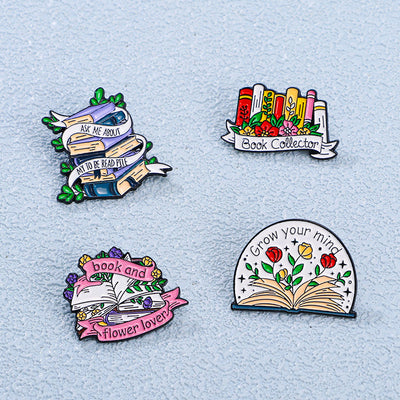 The "Book Collector" Enamel Pin is an adorable, teeny-tiny little enamel pin, featuring a row of stylised books in shades of pink, orange, and red, adorned with flowers and ribbons. So cute! Grab yours today!