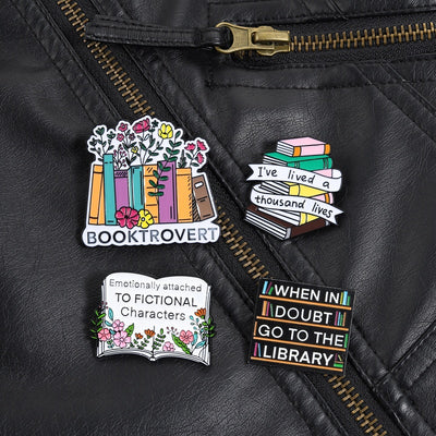 The "Booktrovert" Enamel Pin is a large pin featuring a row of colourful books, adorned with stylised flowers and leaves, with the slogan along the bottom like a bookshelf. Simple, colourful, and lovely! Grab yours today!