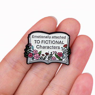The "Emotionally Attached To Fictional Characters" Enamel Pin features a stylised book adorned with delicate leaves and flowers, and text proclaiming your love of certain fictional characters. Oh my! No judgement here!