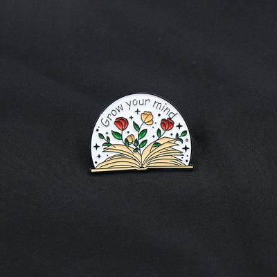 The "Grow Your Mind" Enamel Pin an average-sized brooch featuring a stylised book with flowers and vines sprouting from the pages, and text encouraging you to grow your mind. So true!