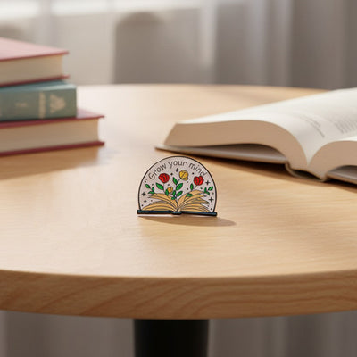 The "Grow Your Mind" Enamel Pin an average-sized brooch featuring a stylised book with flowers and vines sprouting from the pages, and text encouraging you to grow your mind. So true!