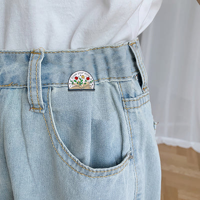 The "Grow Your Mind" Enamel Pin an average-sized brooch featuring a stylised book with flowers and vines sprouting from the pages, and text encouraging you to grow your mind. So true!