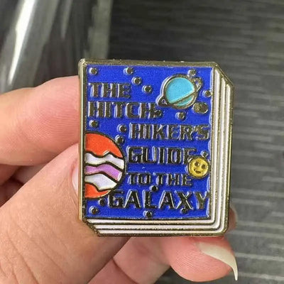 The "Hitchhiker's Guider" Enamel Pin features a stylised replica of the cult classic book, The Hitchhiker's Guide To The Galaxy, in vibrant coloured enamel paint, edged with metallic gold.