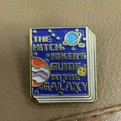 The "Hitchhiker's Guider" Enamel Pin features a stylised replica of the cult classic book, The Hitchhiker's Guide To The Galaxy, in vibrant coloured enamel paint, edged with metallic gold.