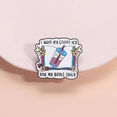 The "I Want My Coffee Icy And My Books Spicy" Enamel Pin features a stylised cup of iced coffee atop a book, adorned with colourful flowers and leaves.