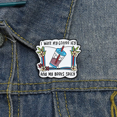 The "I Want My Coffee Icy And My Books Spicy" Enamel Pin features a stylised cup of iced coffee atop a book, adorned with colourful flowers and leaves.