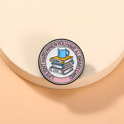 The "Life Isn't Hard When You Have A Library Card" Enamel Pin features a stack of books in the centre (plus a cup of sweet, sweet coffee!), within a ring of text proclaiming your love for libraries.