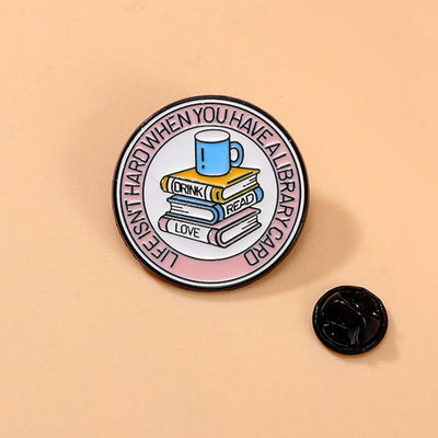 The "Life Isn't Hard When You Have A Library Card" Enamel Pin features a stack of books in the centre (plus a cup of sweet, sweet coffee!), within a ring of text proclaiming your love for libraries.