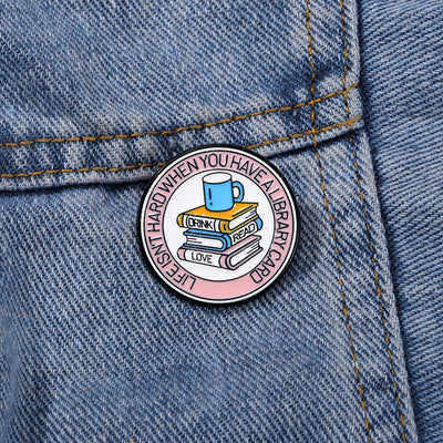 The "Life Isn't Hard When You Have A Library Card" Enamel Pin features a stack of books in the centre (plus a cup of sweet, sweet coffee!), within a ring of text proclaiming your love for libraries.
