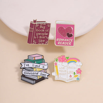 The "Live Your Most Creative Life" Enamel Pin is an average-sized brooch featuring a stylised book, decorated with flowers, rainbow, and art supplies. Perfect for the creative soul!