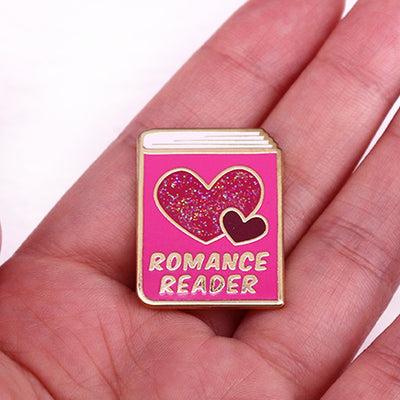 The "Romance Reader" Enamel Pin is a simple but elegant design, featuring a pink book outlined in gold, adorned with hearts. Perfect for expressing your love of the romance genre to all. Grab yours today!