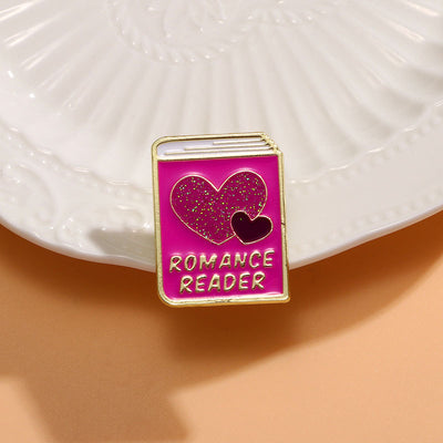 The "Romance Reader" Enamel Pin is a simple but elegant design, featuring a pink book outlined in gold, adorned with hearts. Perfect for expressing your love of the romance genre to all. Grab yours today!