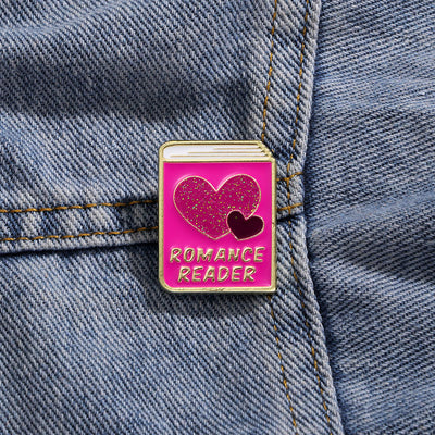 The "Romance Reader" Enamel Pin is a simple but elegant design, featuring a pink book outlined in gold, adorned with hearts. Perfect for expressing your love of the romance genre to all. Grab yours today!