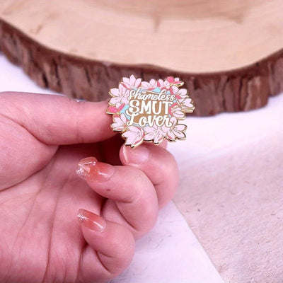 The "Shameless Smut Lover" Enamel Pin features a saucy declaration of your love for naughty romance novels, surrounded by a ring of cute cherry blossoms.