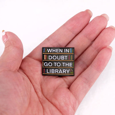 The "When In Doubt Go To The Library" Enamel Pin a large pin featuring a stylised bookshelf covered in books, and lettering proclaiming your love of all things library-related.