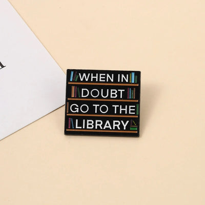 The "When In Doubt Go To The Library" Enamel Pin a large pin featuring a stylised bookshelf covered in books, and lettering proclaiming your love of all things library-related.