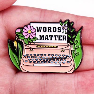 The "Words Matter" Enamel Pin features a stylised typewriter adorned with flowers and leaves, with "Words Matter" printed on the typewriter's paper. So true! They really do!