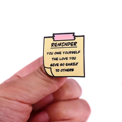 "You Owe Yourself" Enamel Pin - An enamel pin sculpted to look like a yellow post-it note, with the message "Reminder: You owe yourself the love you give so easily to others" on it.