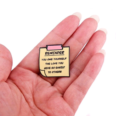"You Owe Yourself" Enamel Pin - An enamel pin sculpted to look like a yellow post-it note, with the message "Reminder: You owe yourself the love you give so easily to others" on it.
