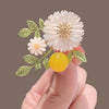 Nadine Daisy Enamel & Shell Brooch - A medium-sized, elegant floral brooch featuring two small stylised daisies, leaves, and a yellow ball.