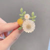 Nadine Daisy Enamel & Shell Brooch - A medium-sized, elegant floral brooch featuring two small stylised daisies, leaves, and a yellow ball.