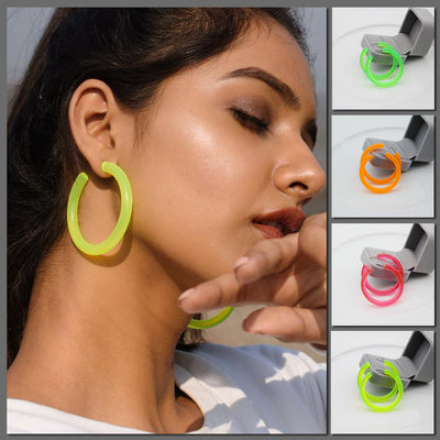 A woman wearing the Neon Vibes Oversized Circular Hoop Earrings, shown in a close-up portrait with four smaller product thumbnails on the right displaying the earring in green, orange, pink, and neon yellow.