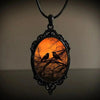 Sunset Ravens Cameo Necklace - A large gothic glass cabochon featuring an image of two silhouetted ravens or crows against a vibrant orange background.