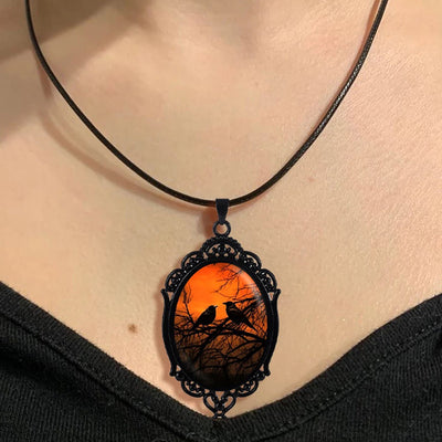 Sunset Ravens Cameo Necklace - A large gothic glass cabochon featuring an image of two silhouetted ravens or crows against a vibrant orange background.