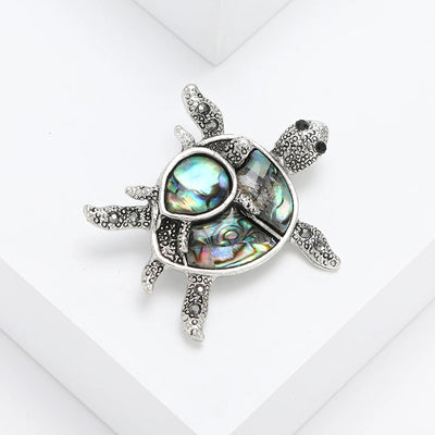 The Tropicana Honu Turtle Brooch - A beautiful silver-toned zinc alloy turtle brooch adorned with crystals and polished paua shell.