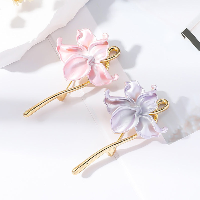 The Gwendolyn Lotus Enamel Brooch - A long, slender floral brooch featuring a stylized lotus blossom in subtle shades of pink and purple, and a golden stem. 
