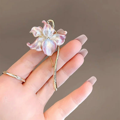 The Gwendolyn Lotus Enamel Brooch - A long, slender floral brooch featuring a stylized lotus blossom in subtle shades of pink and purple, and a golden stem.