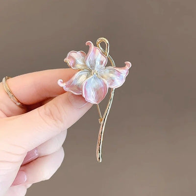 The Gwendolyn Lotus Enamel Brooch - A long, slender floral brooch featuring a stylized lotus blossom in subtle shades of pink and purple, and a golden stem.