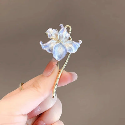 The Gwendolyn Lotus Enamel Brooch - A long, slender floral brooch featuring a stylized lotus blossom in subtle shades of pink and purple, and a golden stem.