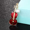 Violin Virtuoso Brooch - A red and gold coloured enamel brooch shaped like a violin, adorned with a large pearl.