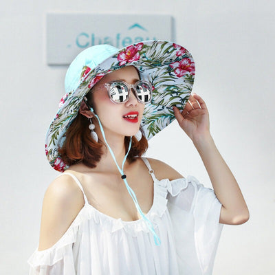 Caribbean Cruise Reversible Sunhat - A large-brimmed, floppy sunhat with a solid colour on one side and a vibrant floral print on the other, which can be worn either way depending on the user's choice. It is decorated with a large removable bow. This image shows a model wearing the Blue colour, which is a very soft baby blue, almost a cyan.