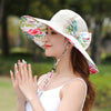 Caribbean Cruise Reversible Sunhat - A large-brimmed, floppy sunhat with a solid colour on one side and a vibrant floral print on the other, which can be worn either way depending on the user's choice. It is decorated with a large removable bow. This image shows a model wearing the Cream colour, which is a fairly standard slightly-off-white creamy colour.
