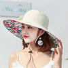 Caribbean Cruise Reversible Sunhat - A large-brimmed, floppy sunhat with a solid colour on one side and a vibrant floral print on the other, which can be worn either way depending on the user's choice. It is decorated with a large removable bow. This image shows a model wearing the Cream colour, which is a fairly standard slightly-off-white creamy colour.