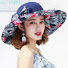 Caribbean Cruise Reversible Sunhat - A large-brimmed, floppy sunhat with a solid colour on one side and a vibrant floral print on the other, which can be worn either way depending on the user's choice. It is decorated with a large removable bow. This image shows a model wearing the Navy colour, which is a very dark blue. The floral print also has a dark blue background.