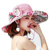Caribbean Cruise Reversible Sunhat - A large-brimmed, floppy sunhat with a solid colour on one side and a vibrant floral print on the other, which can be worn either way depending on the user's choice. It is decorated with a large removable bow. This image shows a model wearing the Pink colour, which is a very soft pastel pink shade.